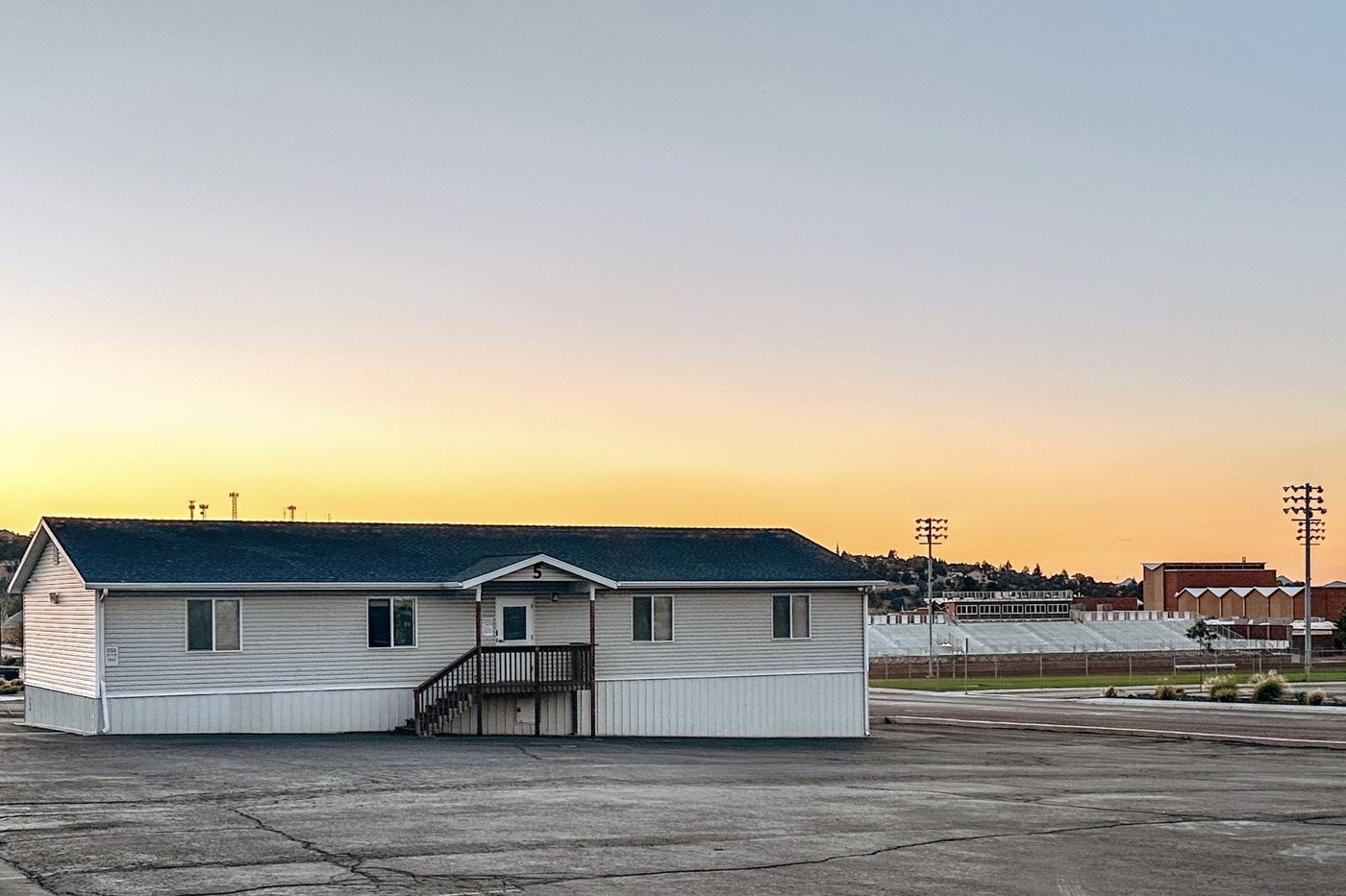 A portable classroom building at dusk in an Iron County school parking lot, with stadium lights behind it.